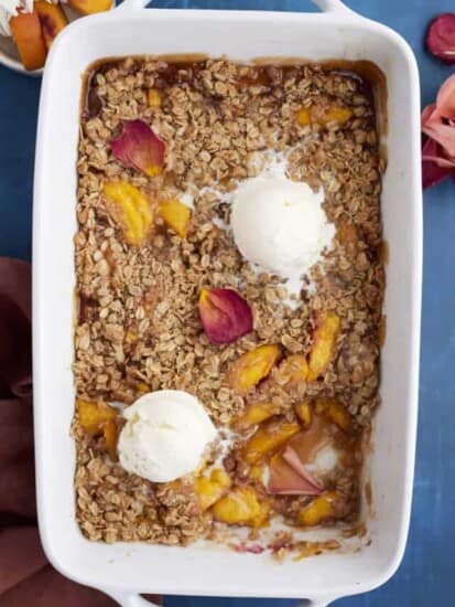 overhead image of a baked peach crisp topped with two scoops of vanilla ice cream with a serving missing out of the bottom righthand corner