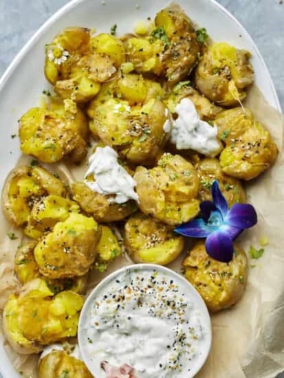 overehead image of smashed potatoes on a serving platter with a side of white creamy sauce.