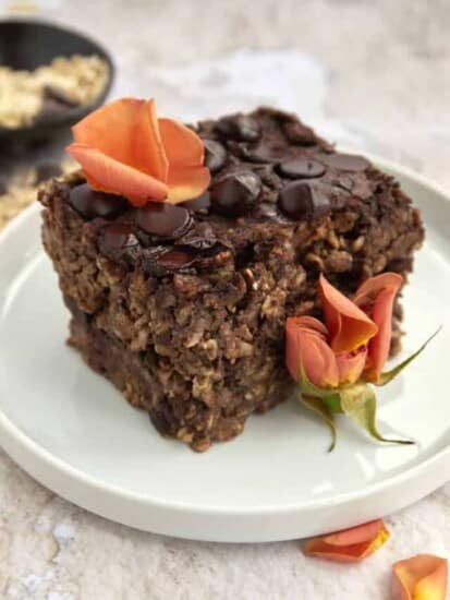 a sliced of chocolate baked oatmeal on a white plate topped with orange flower petals.