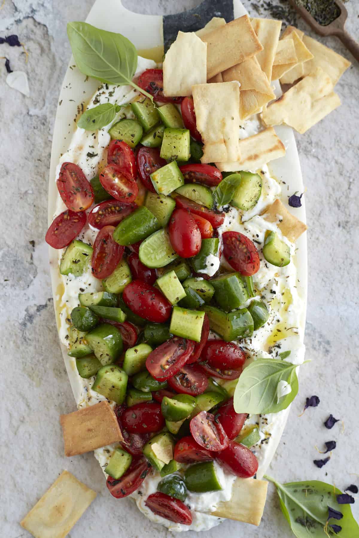 overhead image of cucumber and tomato salad layered over whipped feta dip with pita chips on the side