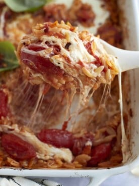 a serving of caprese baked orzo pasta being lifted out of a casserole dish