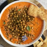 a bowl of feta roasted red pepper dip topped with chickpeas with pita chips on the side