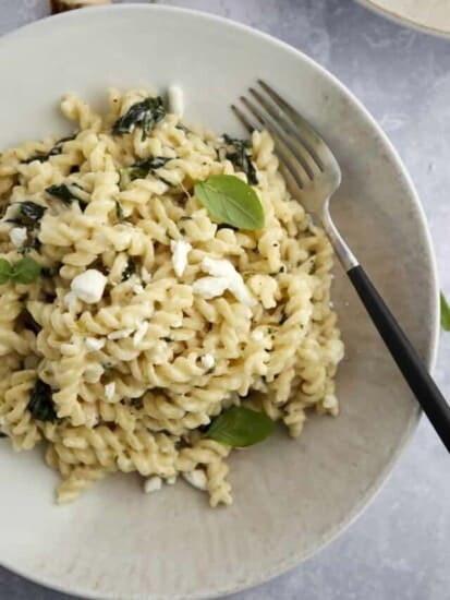 Spanakopita pasta with spinach in a white bowl with a fork on the side