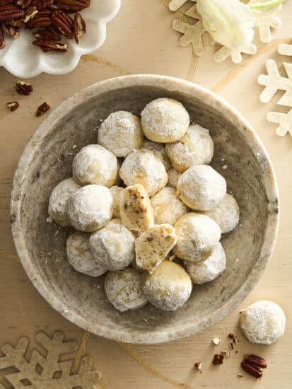 A bowl of pecan snowball cookies, the top cookie split in half.