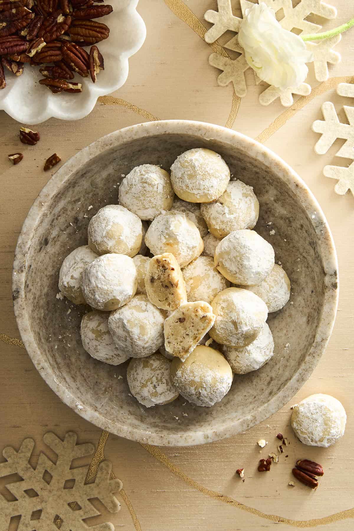 A bowl of pecan snowball cookies, the top cookie split in half.