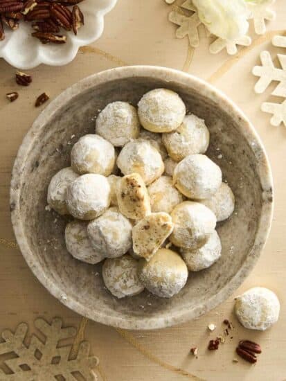 A bowl of pecan snowball cookies, the top cookie split in half.