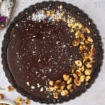 A whole chocolate tart topped with candied hazelnuts and sea salt.