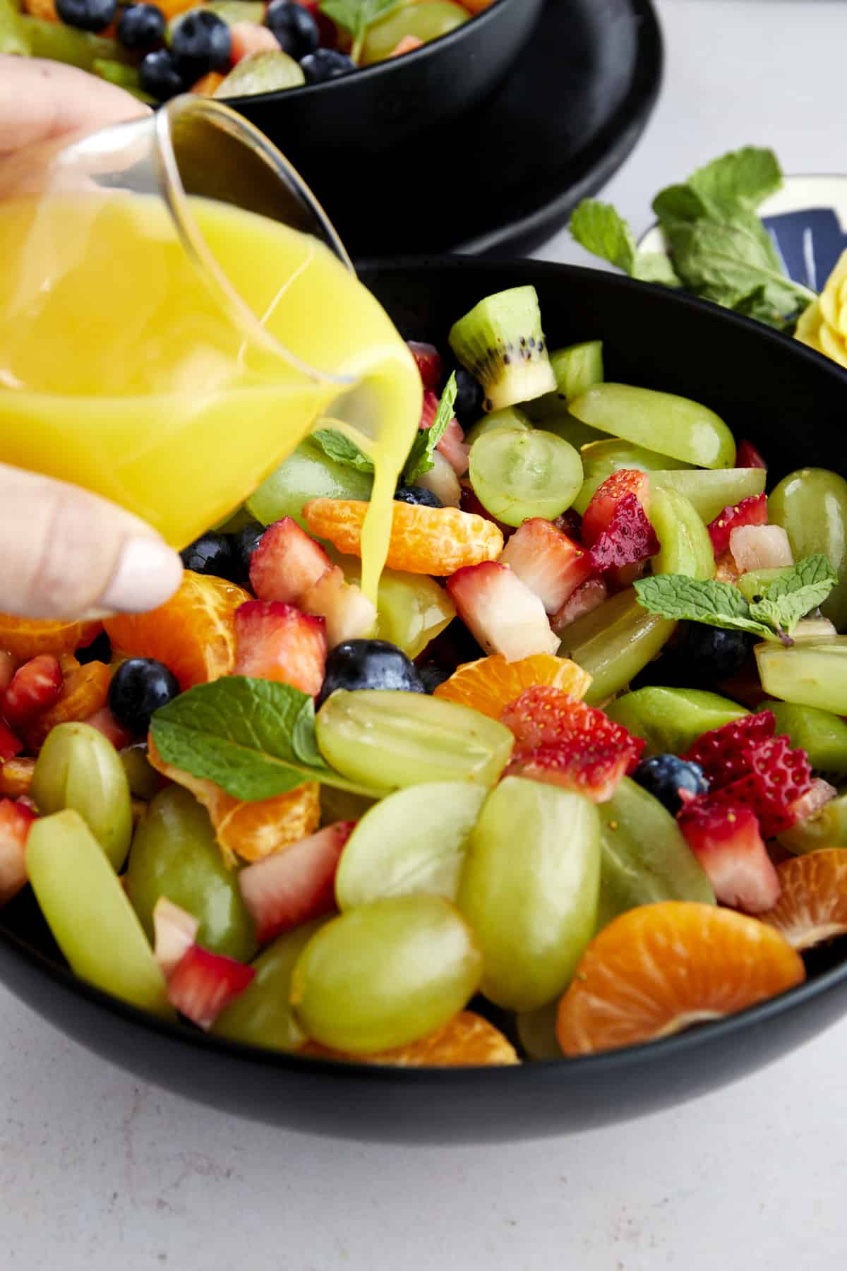 orange juice dressing being poured over a bowl of easy fruit salad