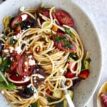 A bowl of Greek spaghetti pasta salad topped with feta with noodle twirled around a fork.