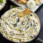 A bowl of crockpot spinach and artichoke dip with a pita chip sticking out.