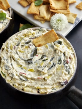 A bowl of crockpot spinach and artichoke dip with a pita chip sticking out.