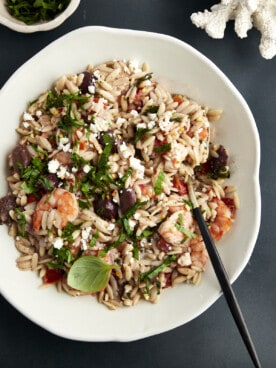 A bowl of shrimp orzo bake topped with fresh herbs with a spoon sticking out.