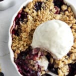 Overhead image of a mixed berry crisp topped with ice cream with a spoon taking a scoop.