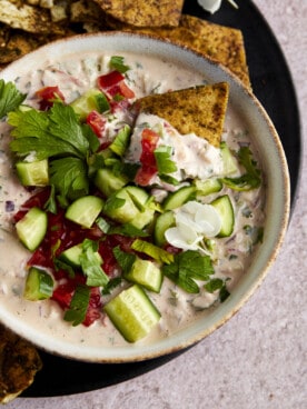 A pita chip dipping into a bowl of tahini salad.