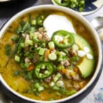 A bowl of healthy white turkey chili topped with sour cream, avocado, jalapeños, and scallions.