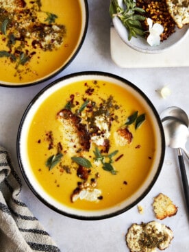 Two bowl of roasted butternut squash soup topped with feta crisps.