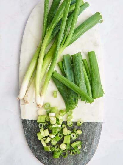 A cutting board with chopped green onions and halved green onions.