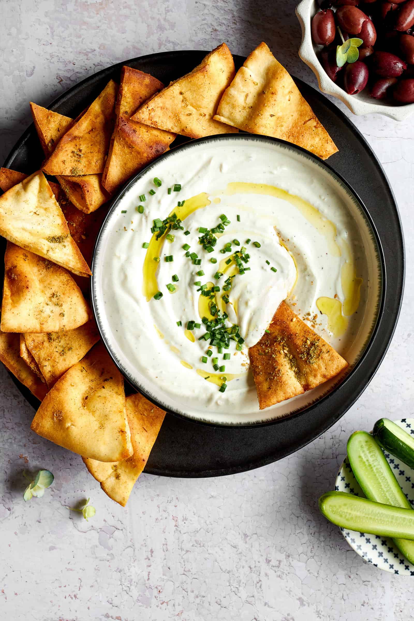 A pita chip dipped into a bowl of garlic yogurt sauce surrounded by more pita chips.