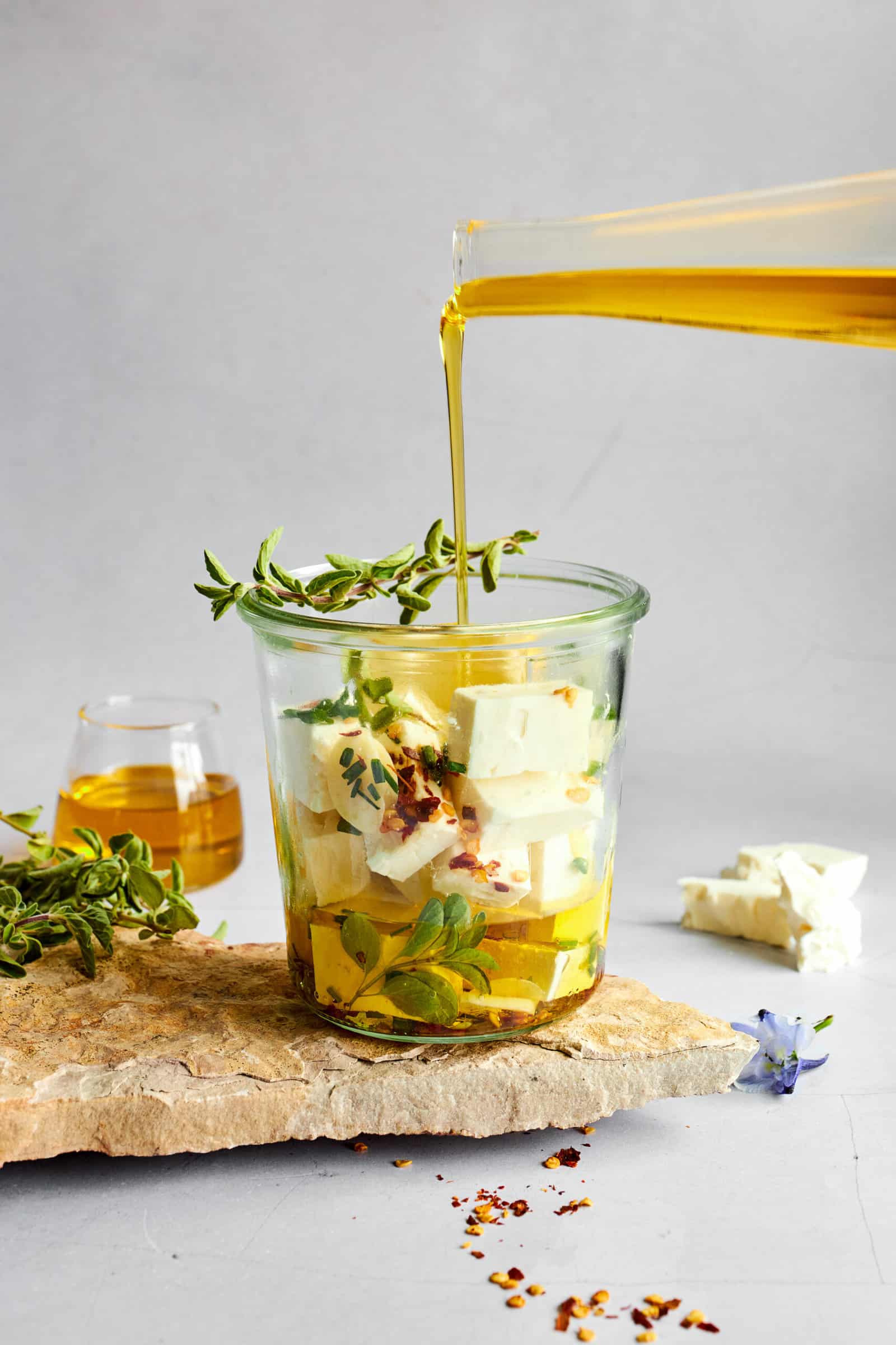 Olive oil being poured over feta cubes in a glass jar.