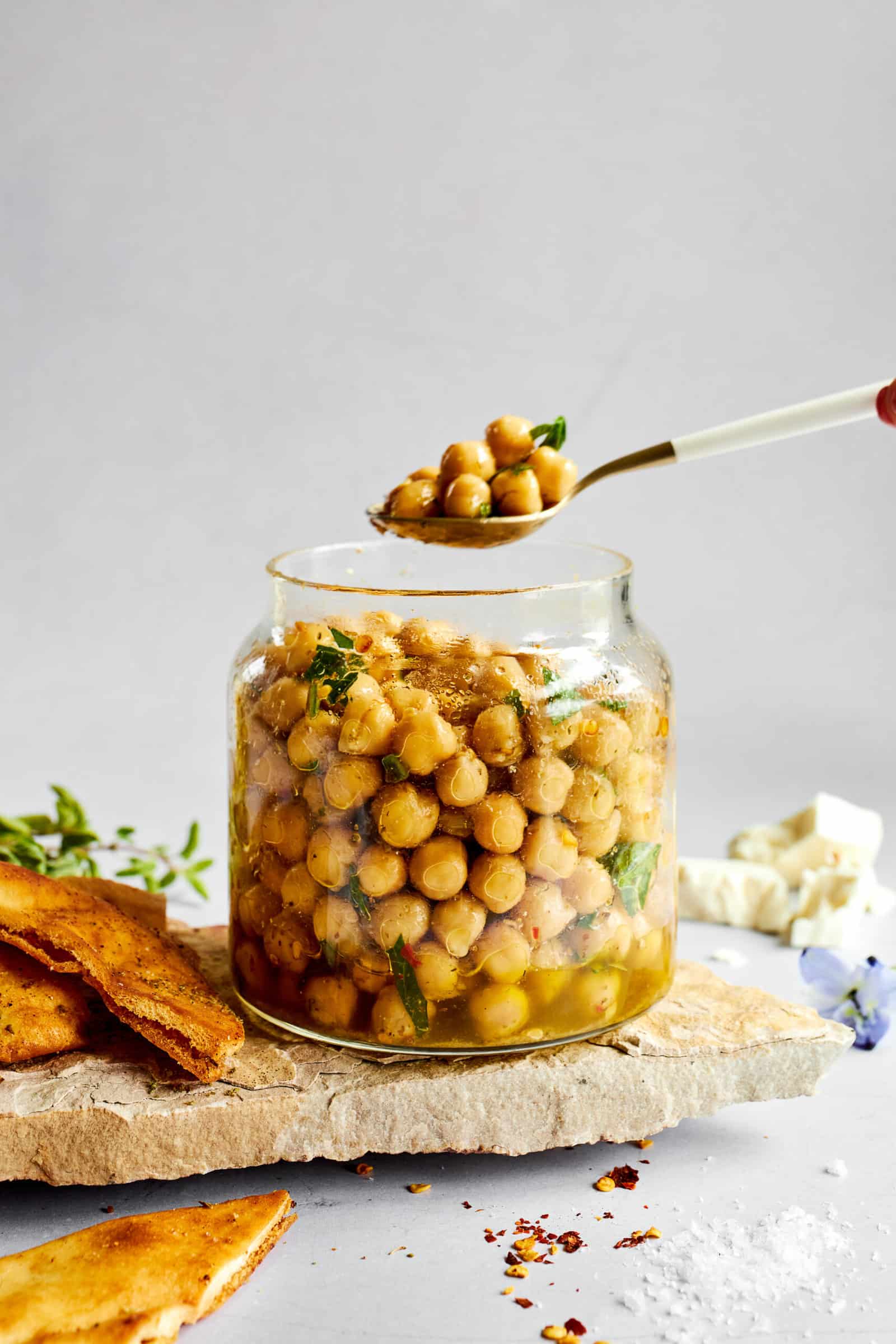 A spoon lifting a scoop of marinated chickpeas from a jar.