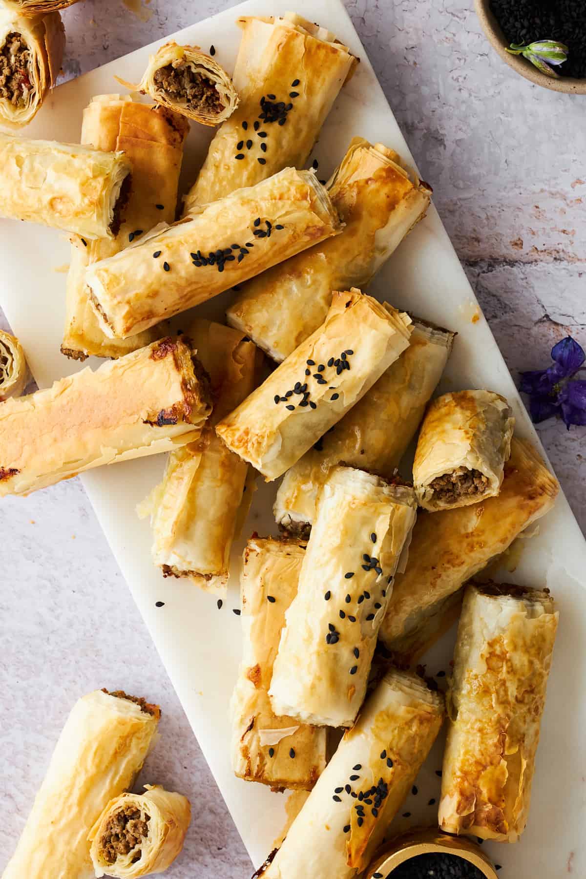 A serving platter full of phyllo rolls with ground beef.