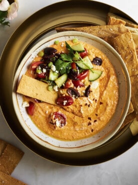 A bowl of spicy feta tip topped with veggies and a cracker.