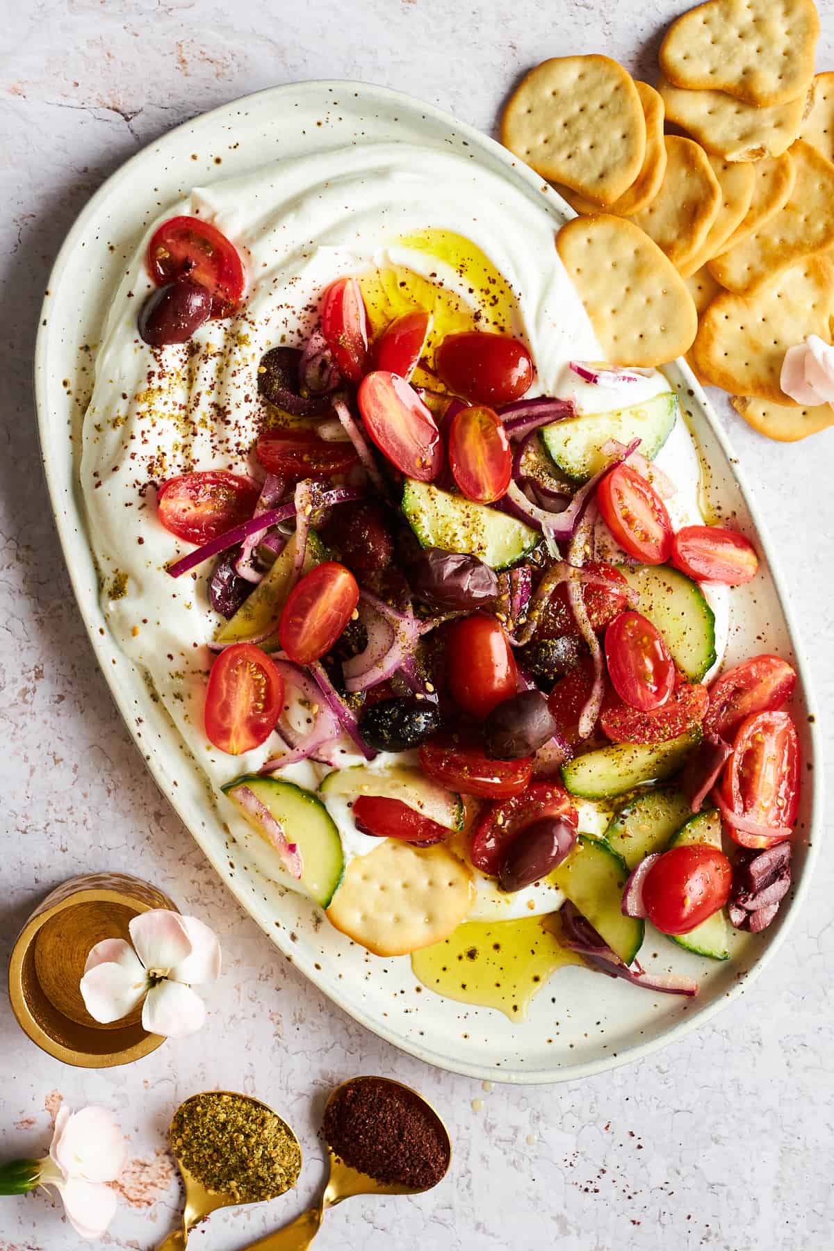 A platter of Greek salad dip with yogurt with crackers on the side. 