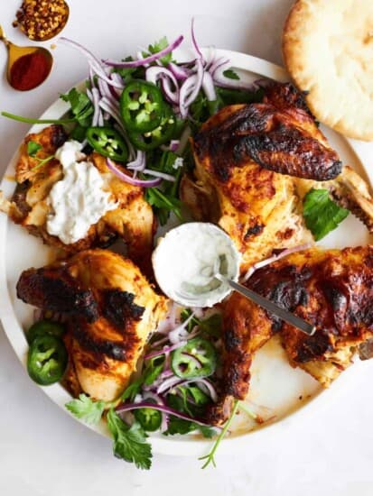 Four pieces of chicken tikka on a plate with garnishes.