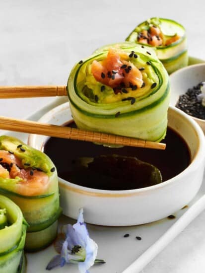 A smoked salmon cucumber roll being dipped in soy sauce.