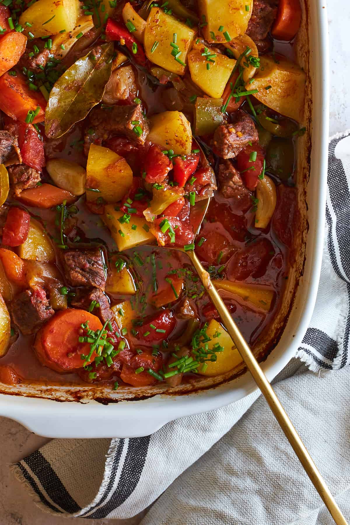 A serving spoon in a casserole dish of baked beef stew.