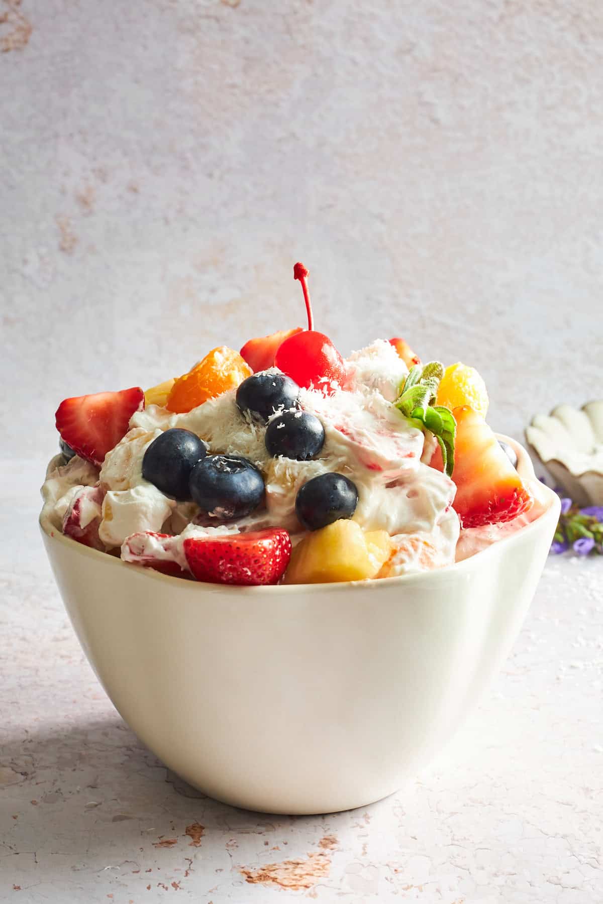 A bowl of ambrosia fruit salad topped with a cherry. 