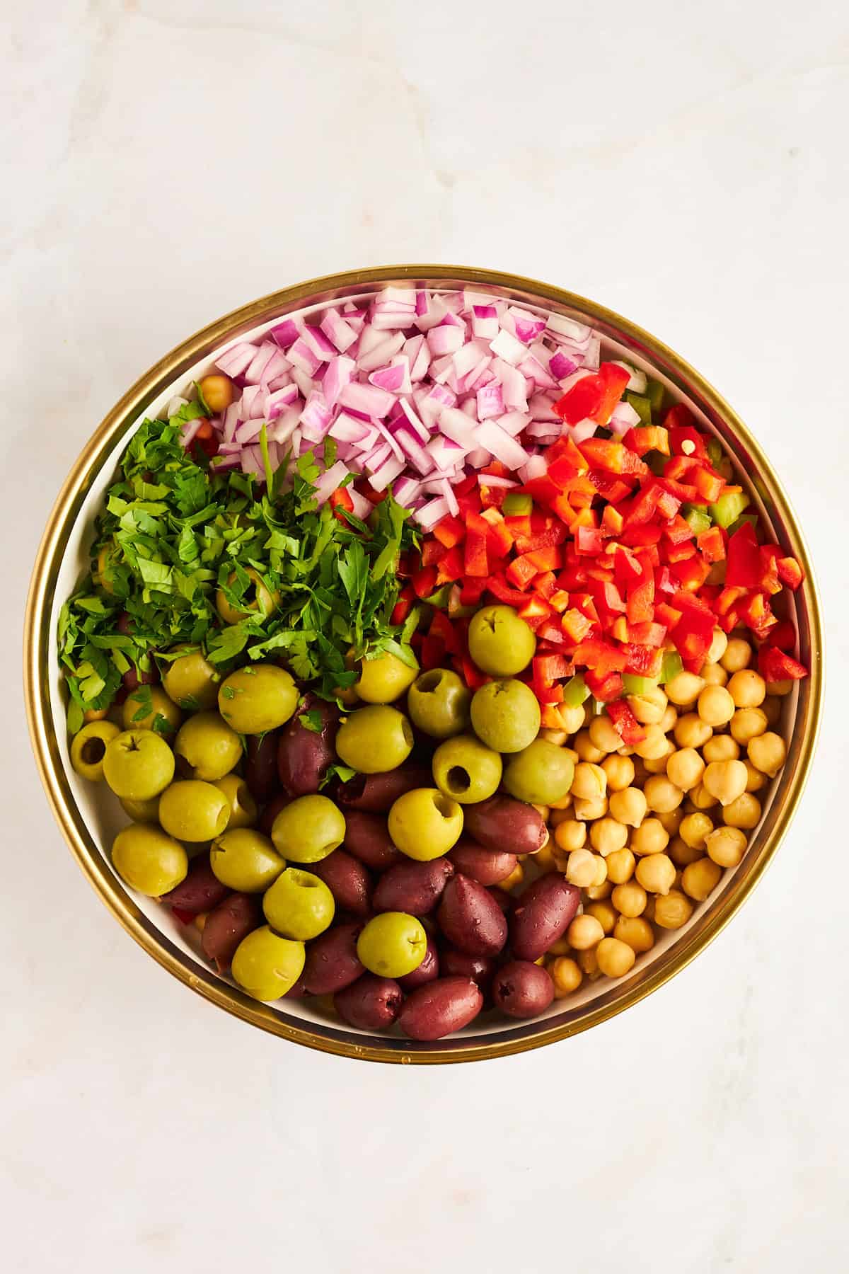 A bowl of red and green olives, fresh herbs, red onion, bell peppers, and chickpeas. 