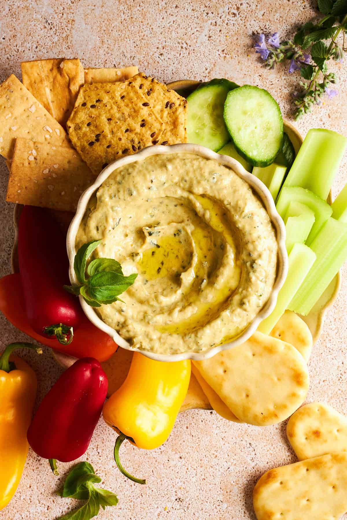 A bowl of zucchini dip on a platter with cucumber, celery, pita, mini bell peppers, and crackers. 