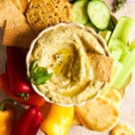 A bowl of zucchini dip with cucumbers, celery, pita, mini bell peppers, and crackers.