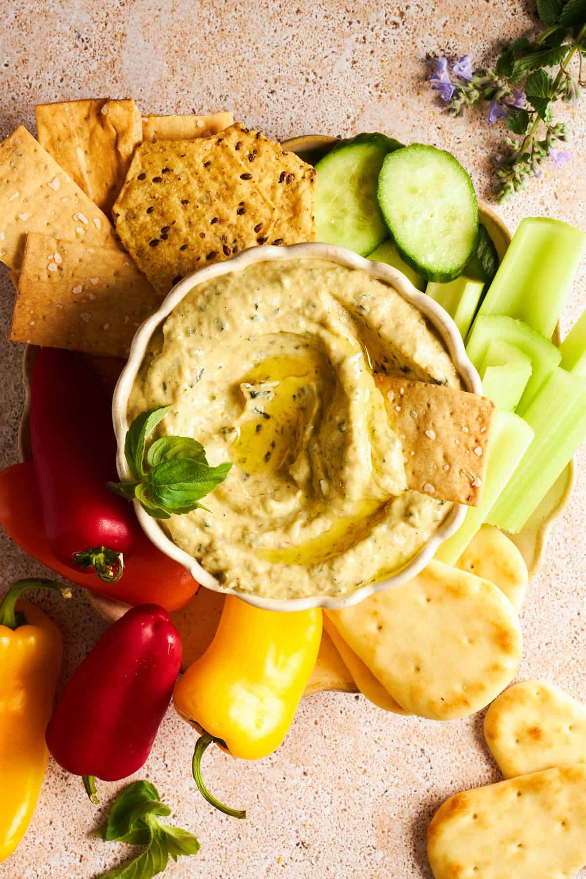 A bowl of zucchini dip with cucumbers, celery, pita, mini bell peppers, and crackers.