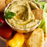 A bowl of zucchini dip with crackers, pita bread, and mini bell peppers.