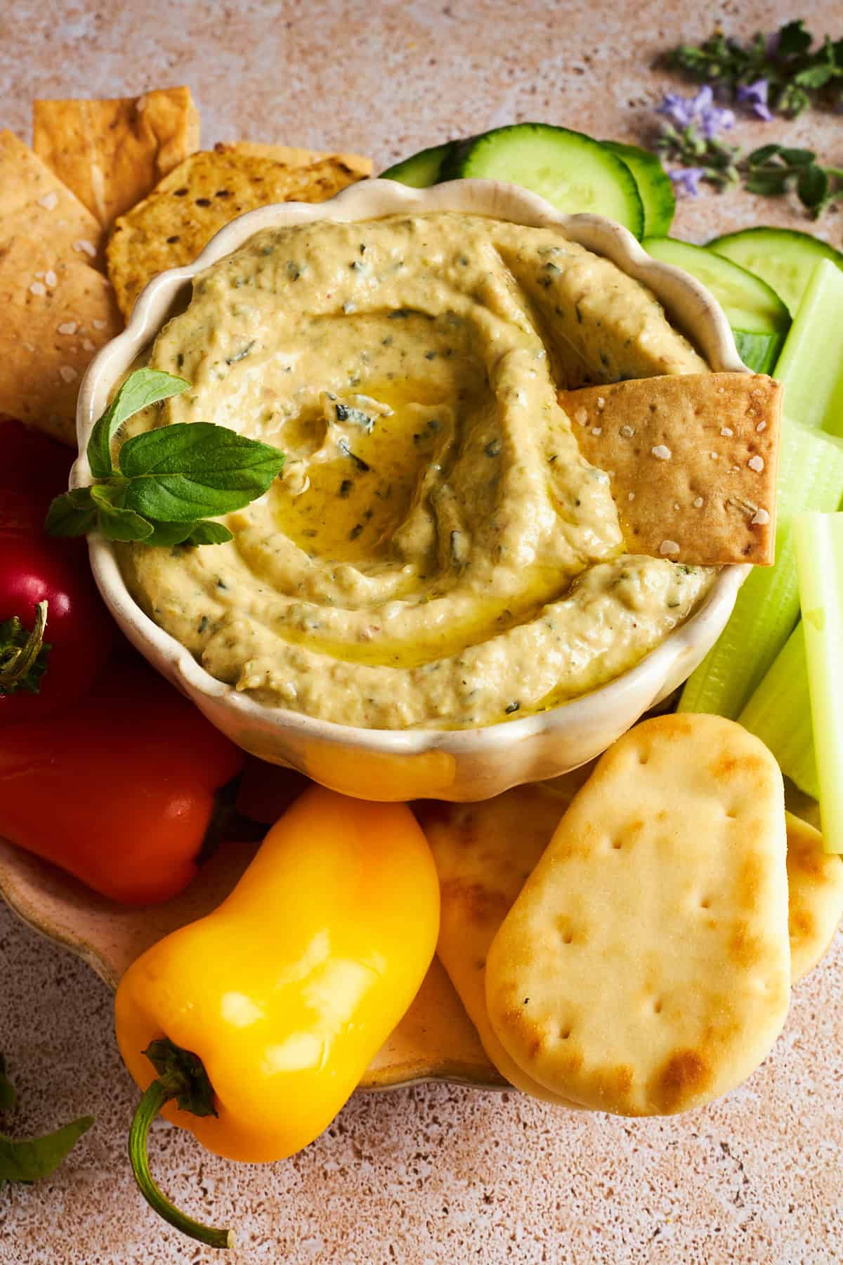A bowl of zucchini dip with crackers, pita bread, and mini bell peppers.