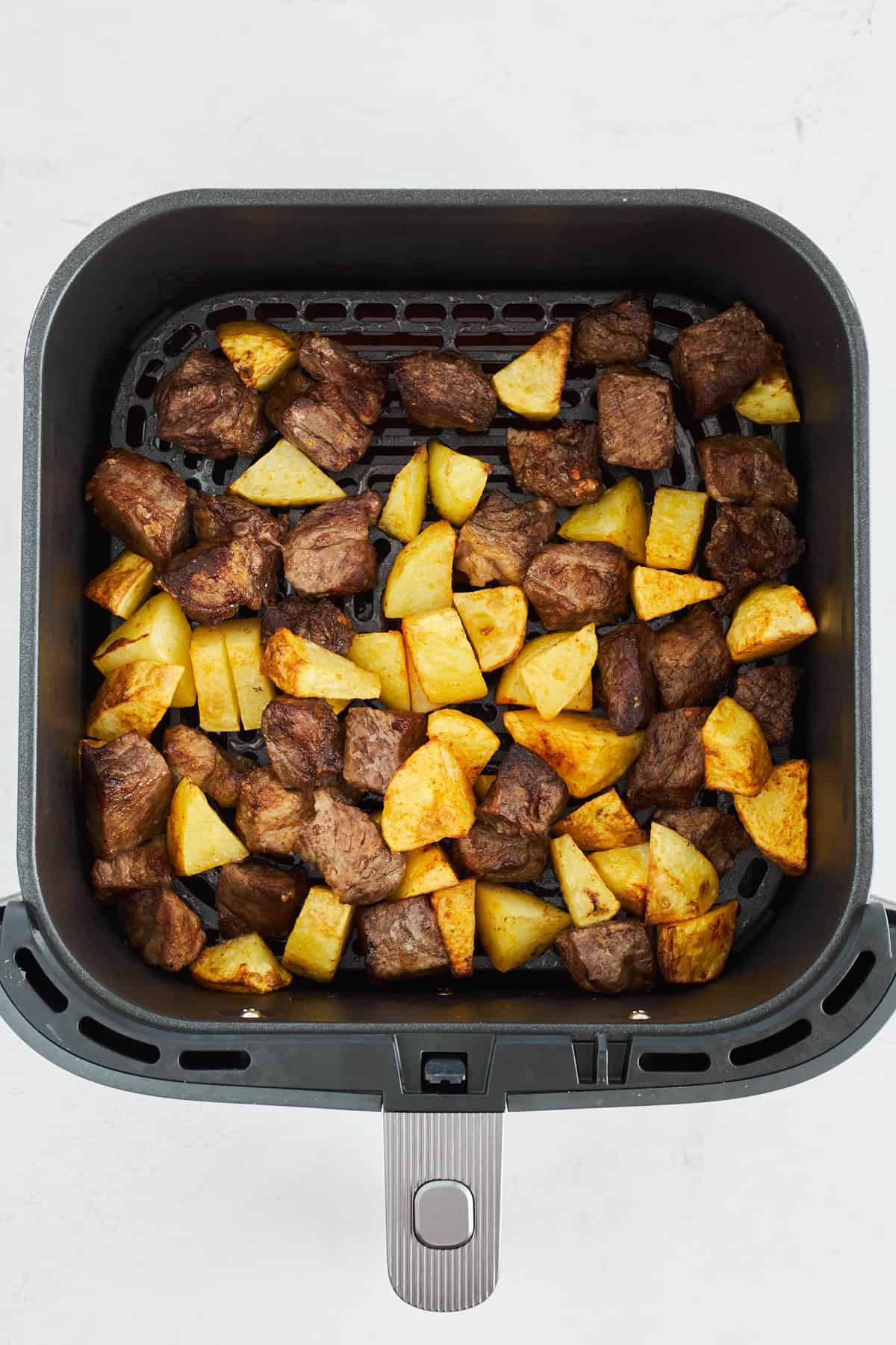 Cooked steak and potato pieces in an air fryer. 