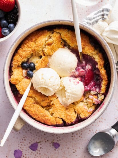 A round dish of mixed berry cobbler topped with three scoops of vanilla ice cream.