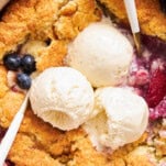 Close up view of mixed berry cobbler topped with three scoops of vanilla ice cream.