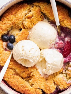 Close up view of mixed berry cobbler topped with three scoops of vanilla ice cream.