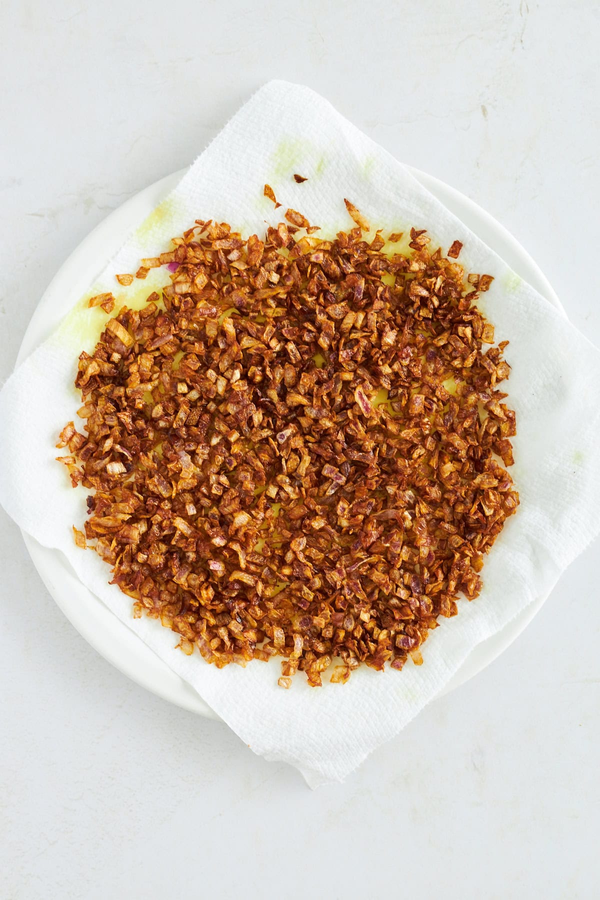 Fried onions draining on a paper towel-lined plate. 