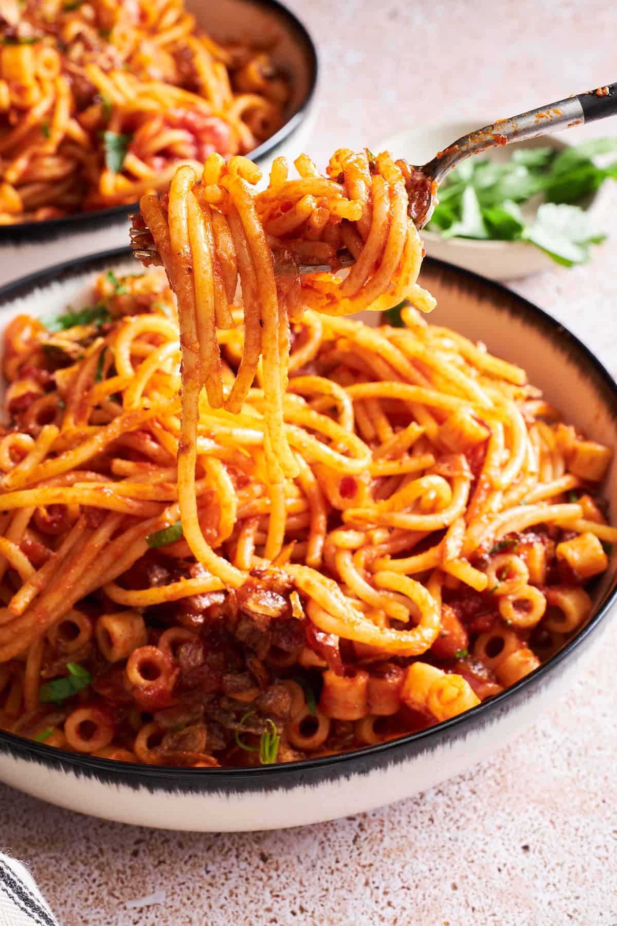 A fork lifting a bite of koshary-inspired Egyptian pasta from a bowl. 