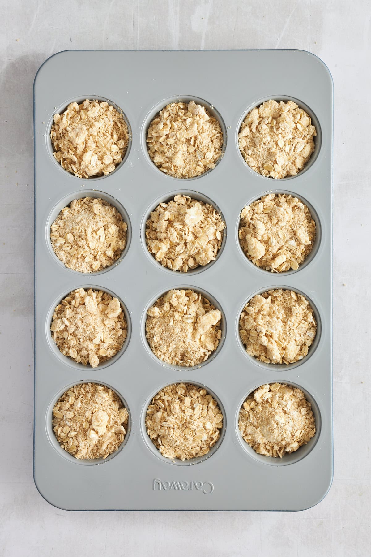Raw dinner rolls topped with an oat crumble in a muffin tin. 