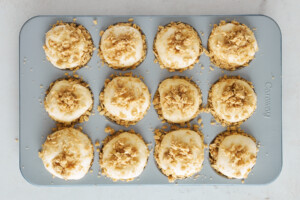 Raw risen dinner rolls in a muffin tin topped with an oat crumble.