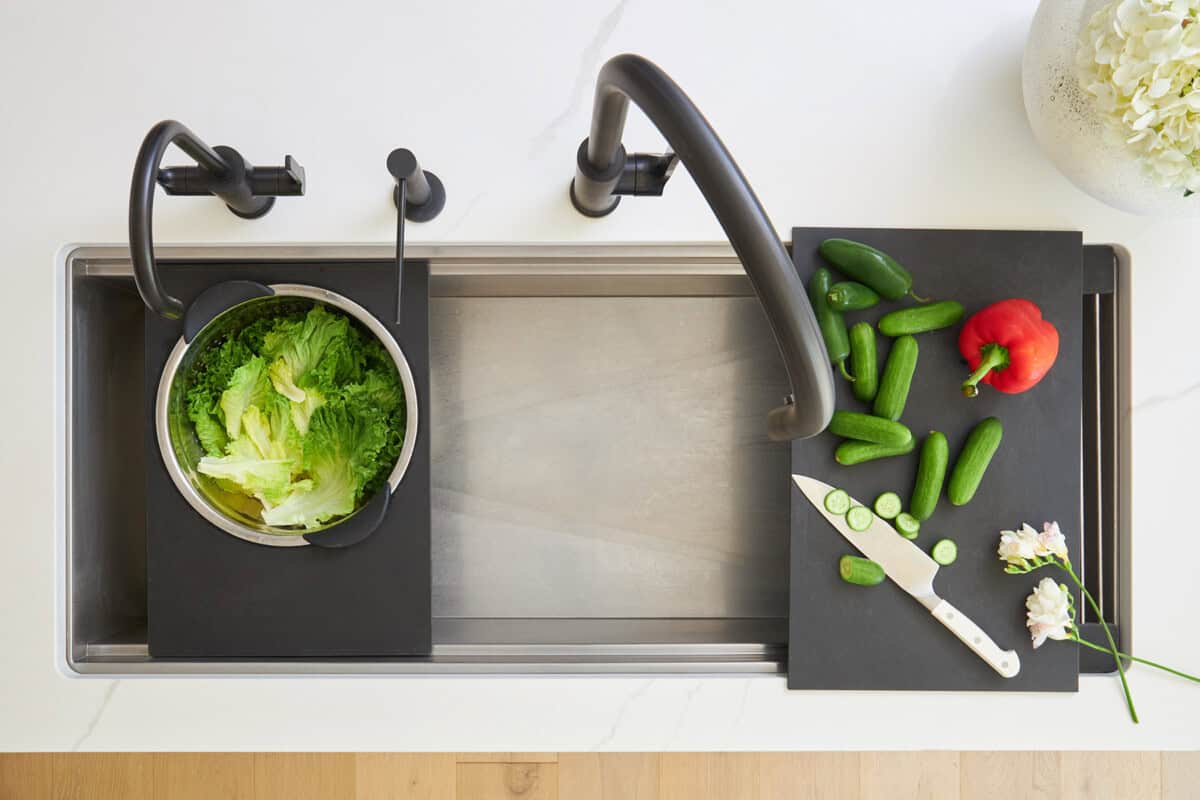 Overhead image of a clean kitchen sink with a colander attachment and a cutting board attachment. 