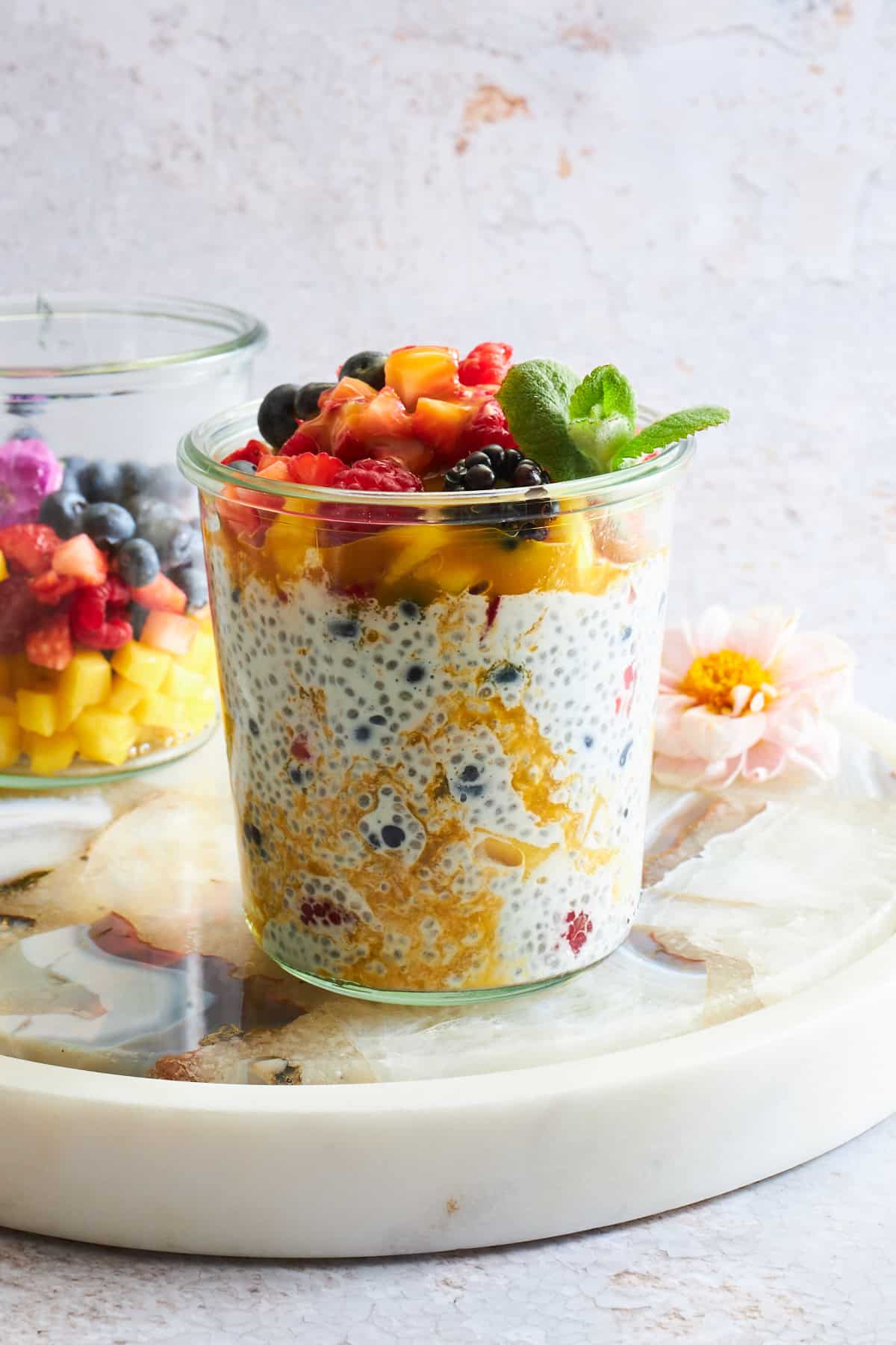 A jar of mango chia pudding topped with fruit salad.