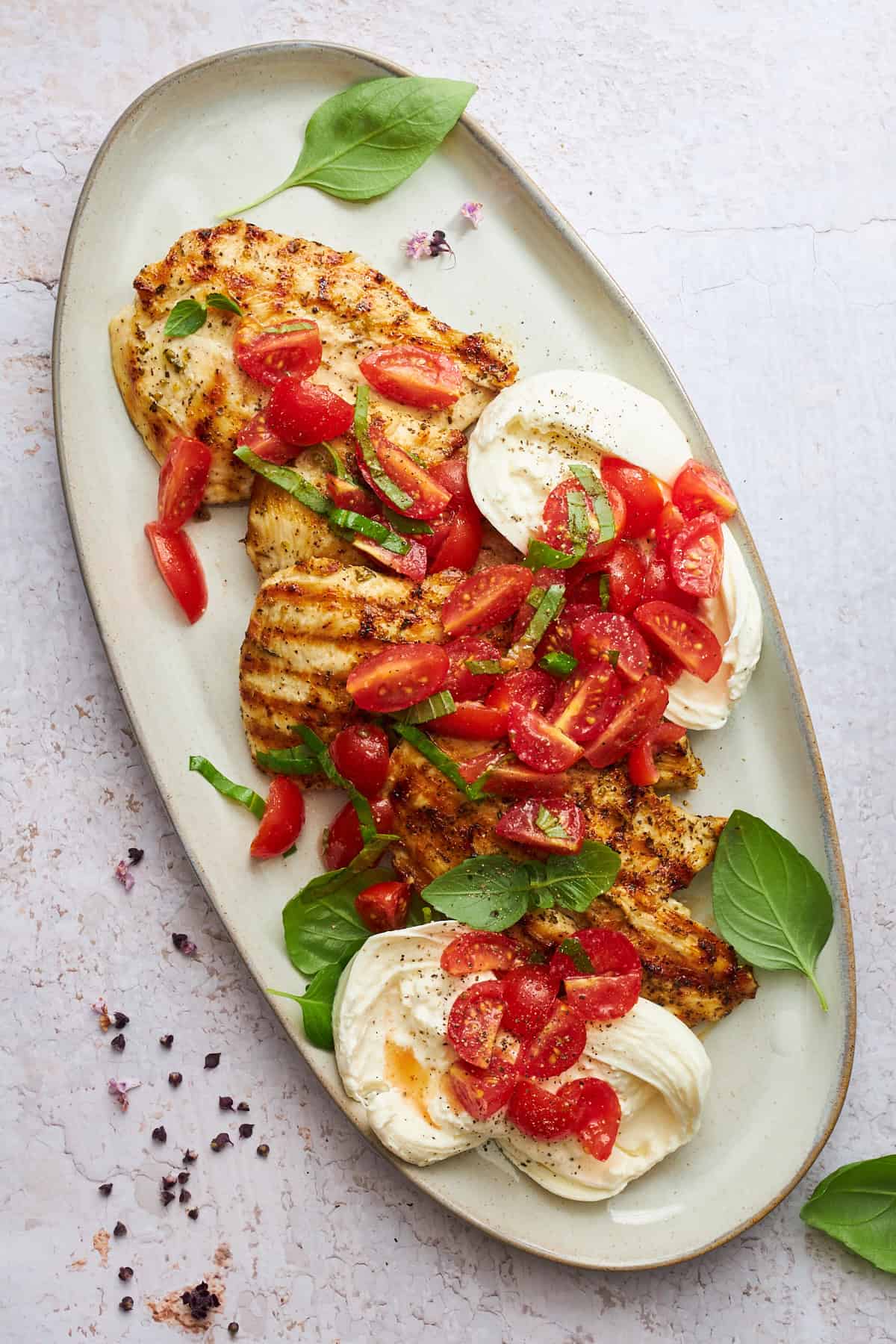A platter of grilled tomato basil chicken with burrata. 