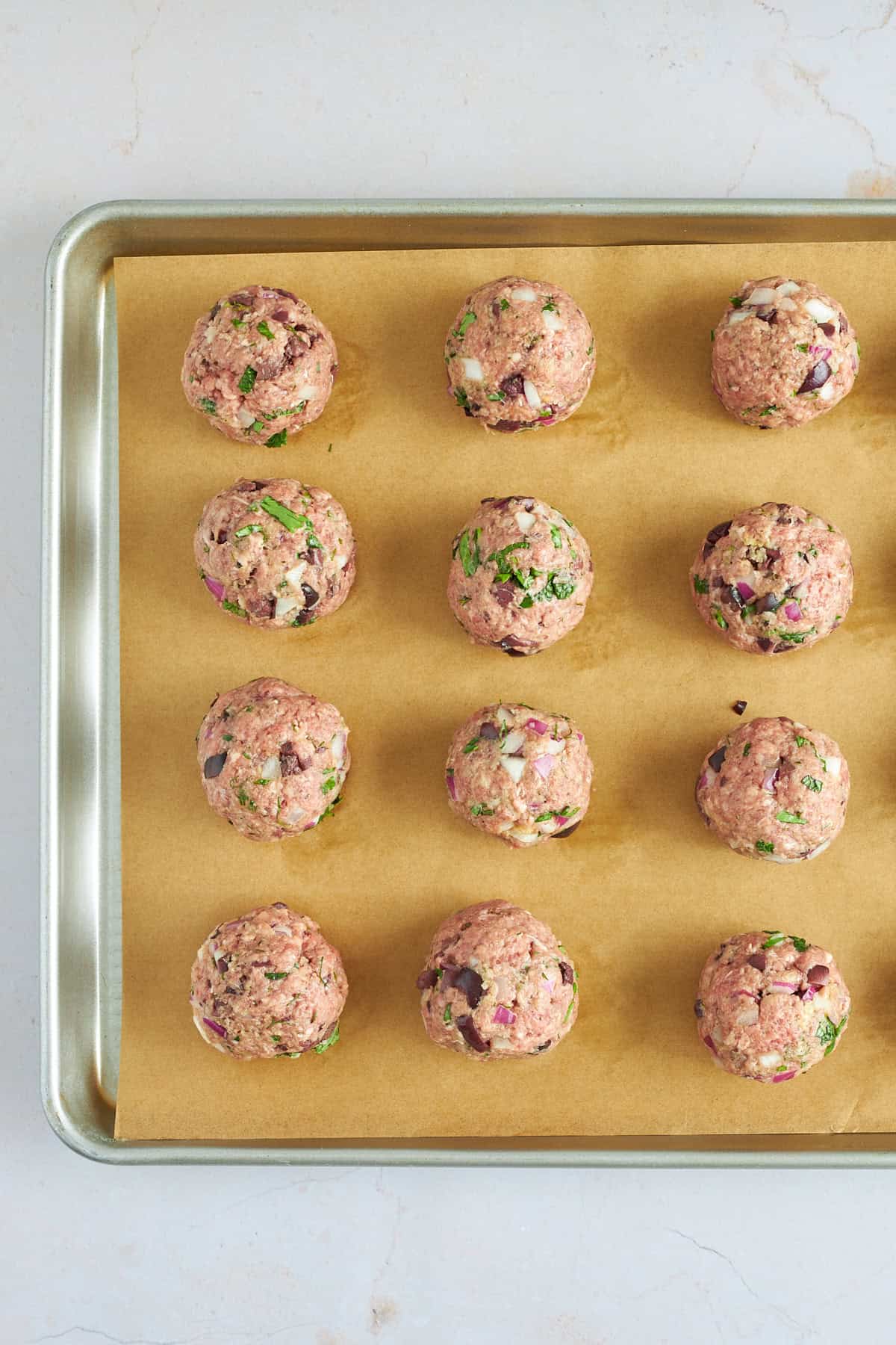 Raw beef meatballs on a baking sheet lined with parchment paper. 