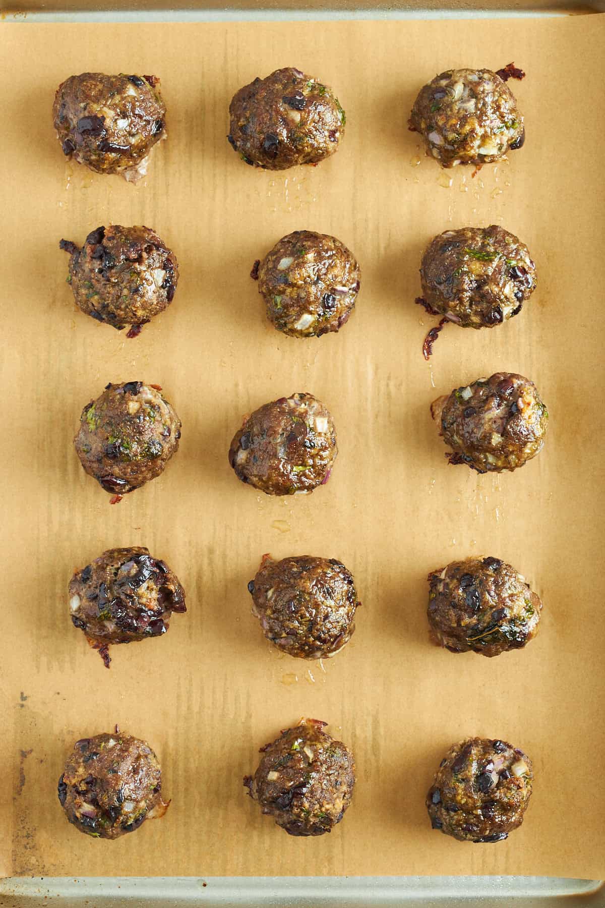 Baked Mediterranean ground beef meatballs on a parchment paper lined baking sheet.